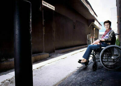 Une dame en fauteuil roulant devant une porte marquée Entrée Handicapés