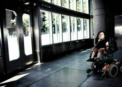 Une personne de petite taille en fauteuil roulant à l'entrée d'une station de métro